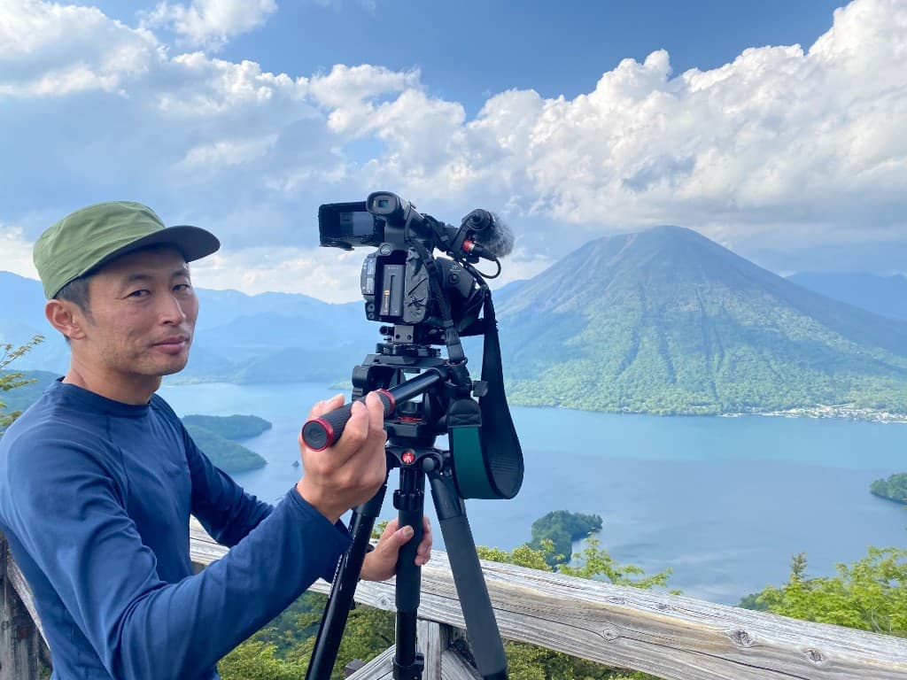 展望台で三脚に据えた業務用カメラを操作する上杉隆寛。背景に湖と山並み